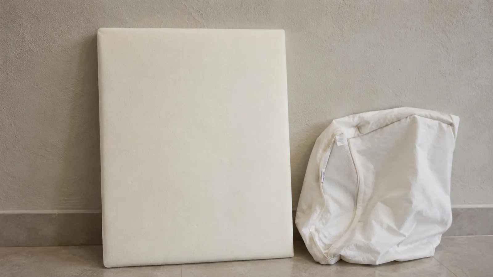A washable pet bed cover leaning beside a thick supportive foam base in a home
